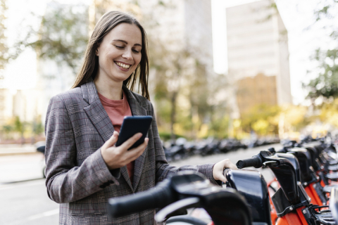 Young businesswoman locks up her city bike while locking in a high return on a certificate on her smartphone.