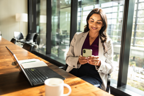Smiling professional woman avoids cybersecurity mistakes on her smartphone and work laptop.