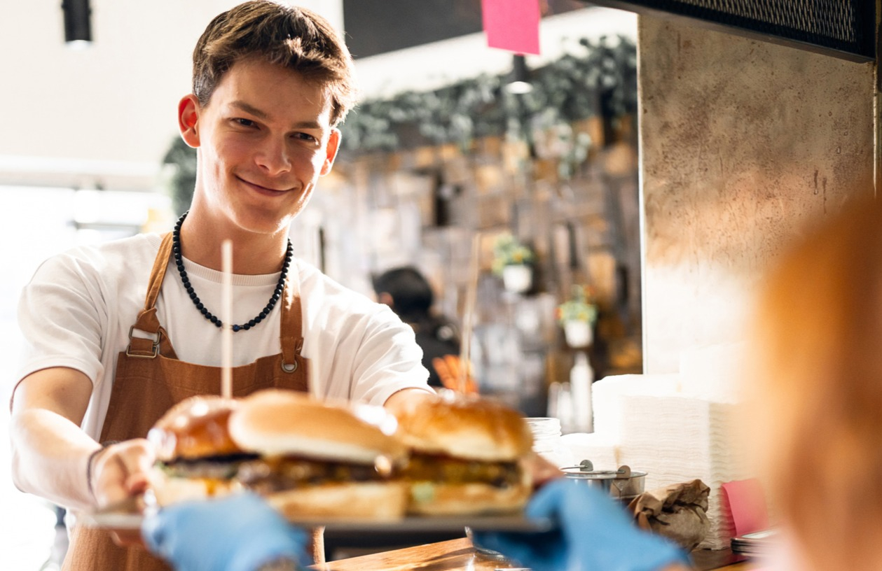 Young man happily works at his summer job in a burger stand.