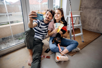 Young couple takes selfie while comparing paint colors for their living room, made affordable by their savings account and certificate. 