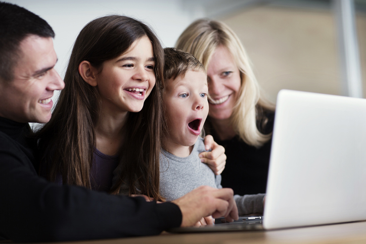 Happy parents and their two children (ages between 5 and 13 years old) open a savings account for kids online together on a laptop. 