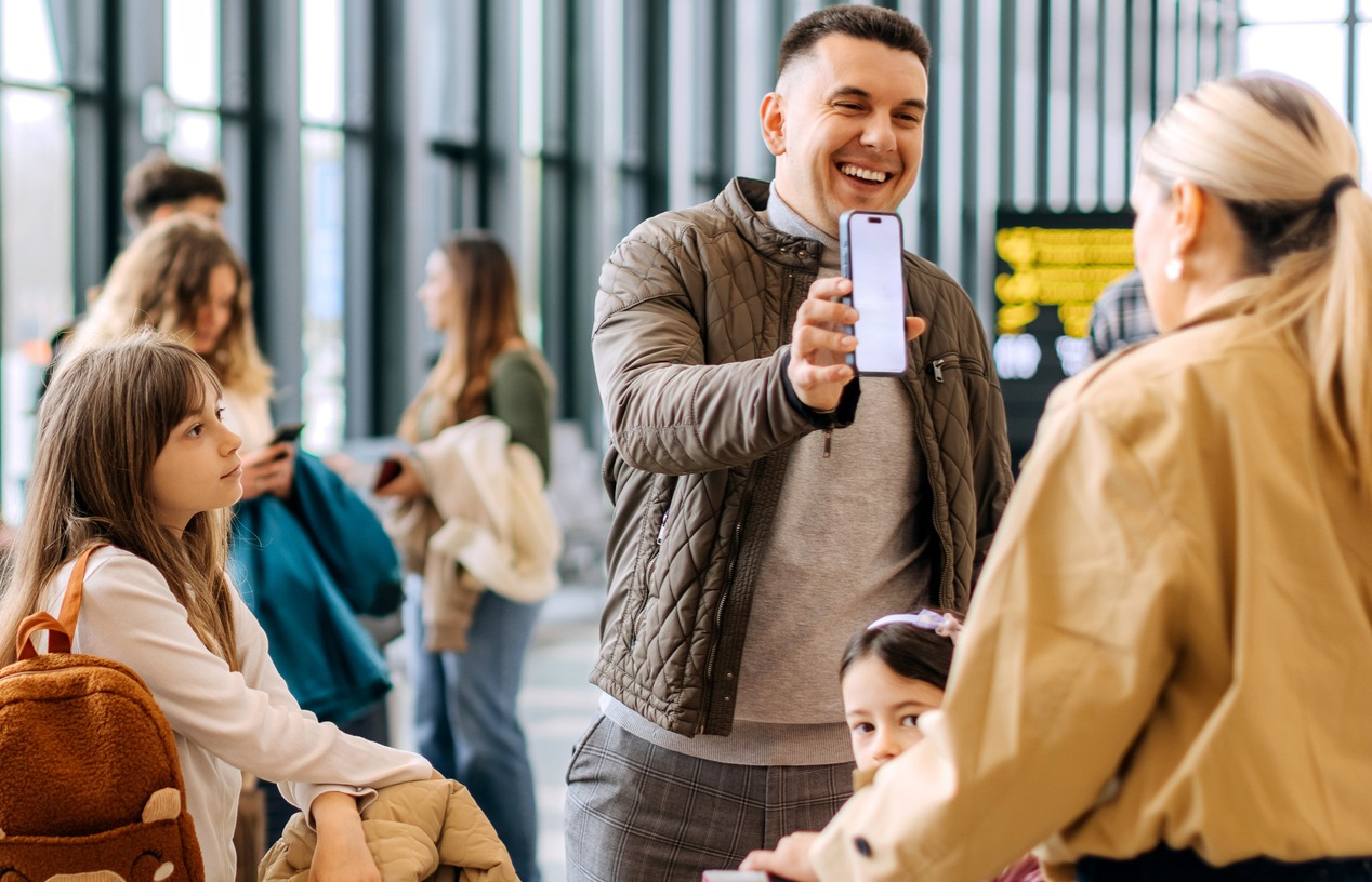 Family travelling on vacation shows wife his accounts on his smartphone while at airport.