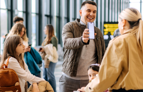 Family travelling on vacation shows wife his accounts on his smartphone while at airport.
