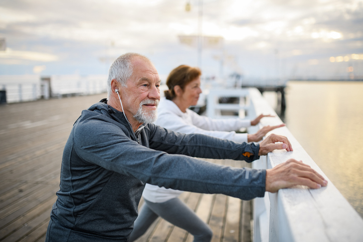 Wealthy older couple stretches on pier by ocean, happily retired with income from their jumbo certificates.
