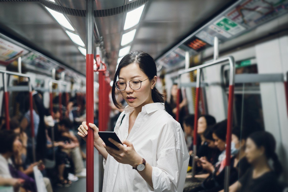 A woman looks at her phone while on the subway