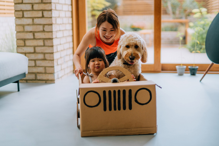 Mother pushes young daughter in toy car in their new home.