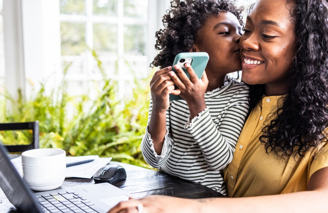 Smiling mother with her young daughter on her lap looks at home equity line of credit (HELOC) closing costs on her laptop.