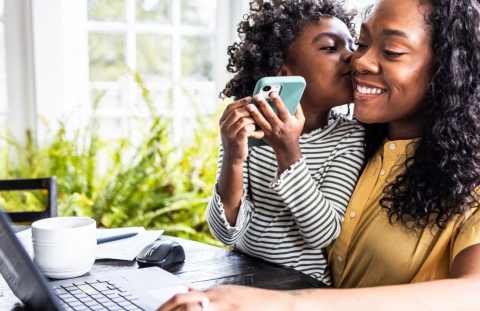 Smiling mother with her young daughter on her lap looks at home equity line of credit (HELOC) closing costs on her laptop.