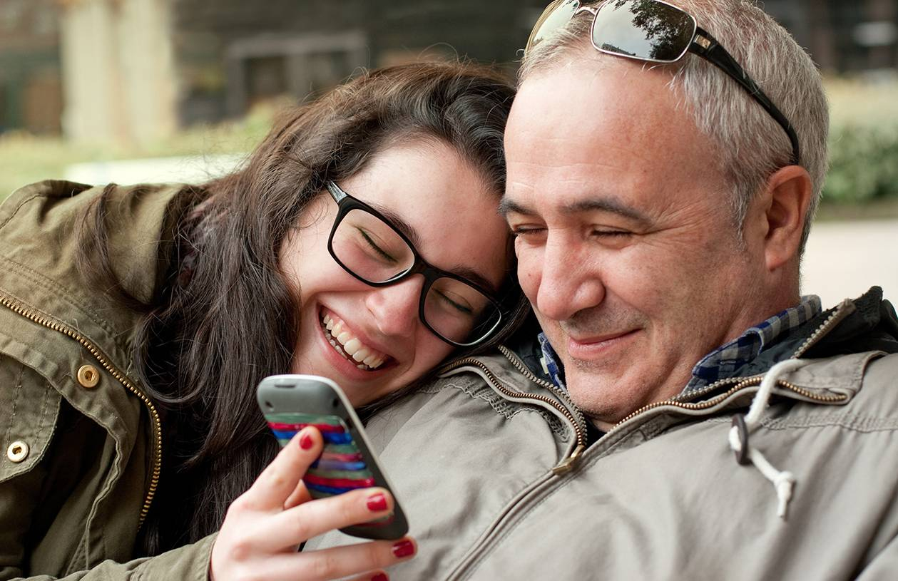 smiling daughter and father looking at mobile phone
