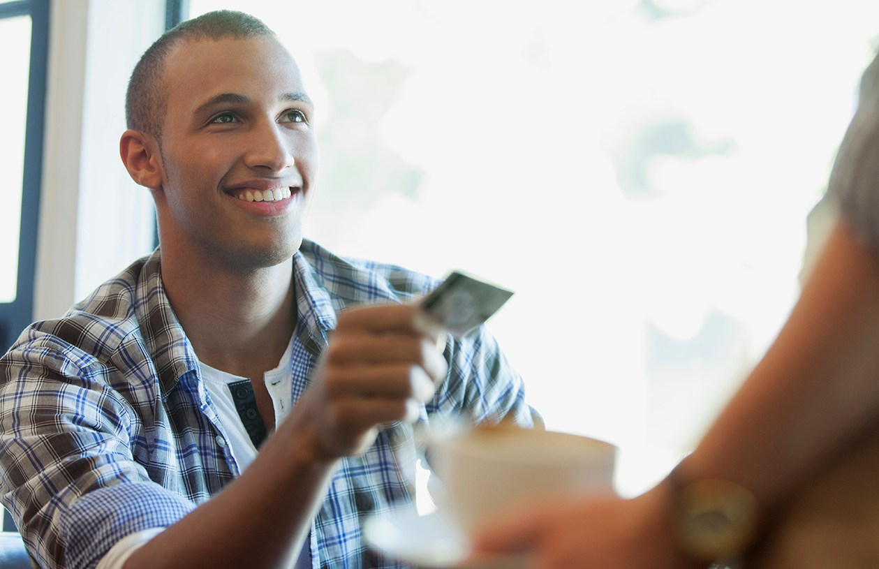 smiling young man pays for coffee using rewards credit card