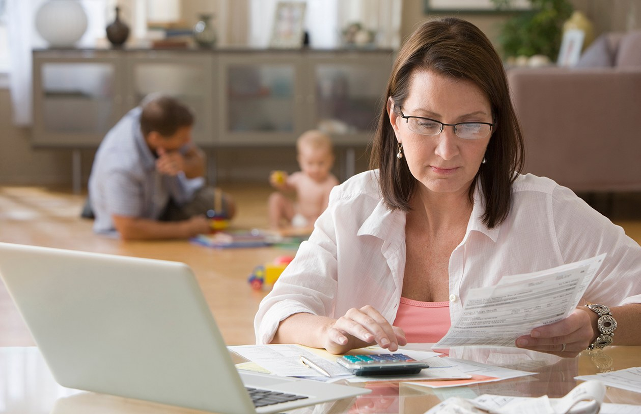 woman sitting at a table doing her finances while her family plays behind her