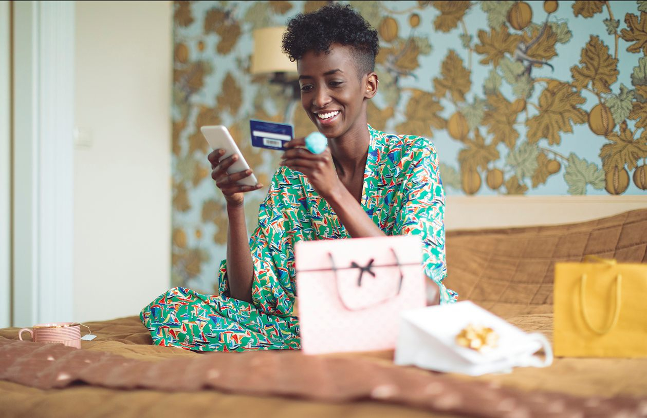 A woman smiles while looking at her credit card and mobile phone