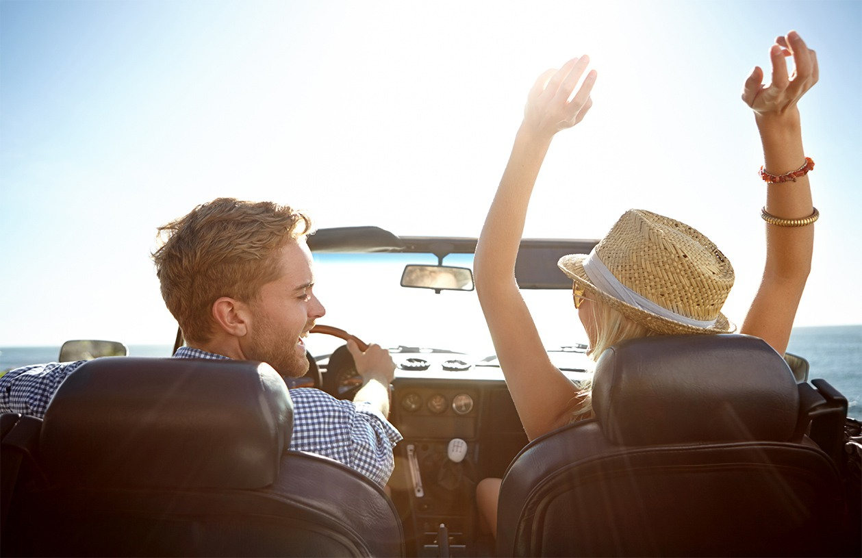 smiling couple driving in convertible  to beach