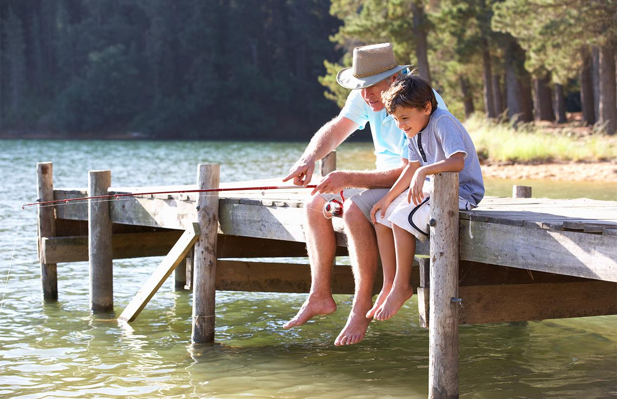 Retired grandfather and young boy sitting on a deck fishing