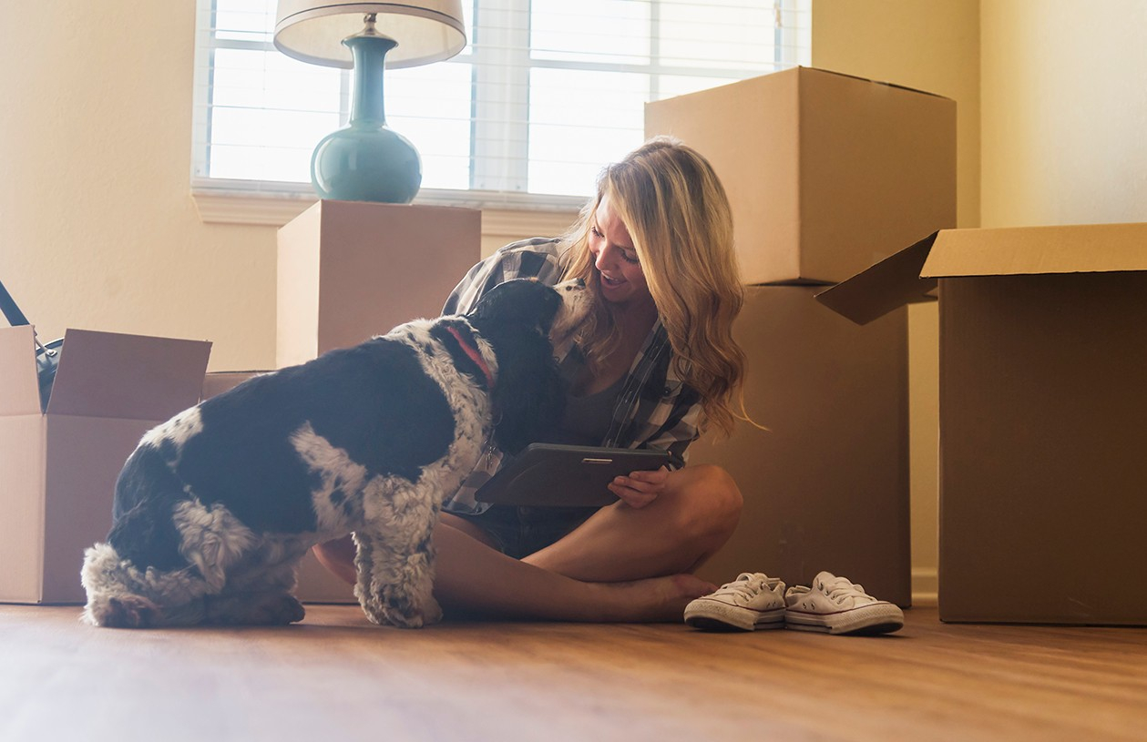 woman with dog surrounded by boxes after moving into new home
