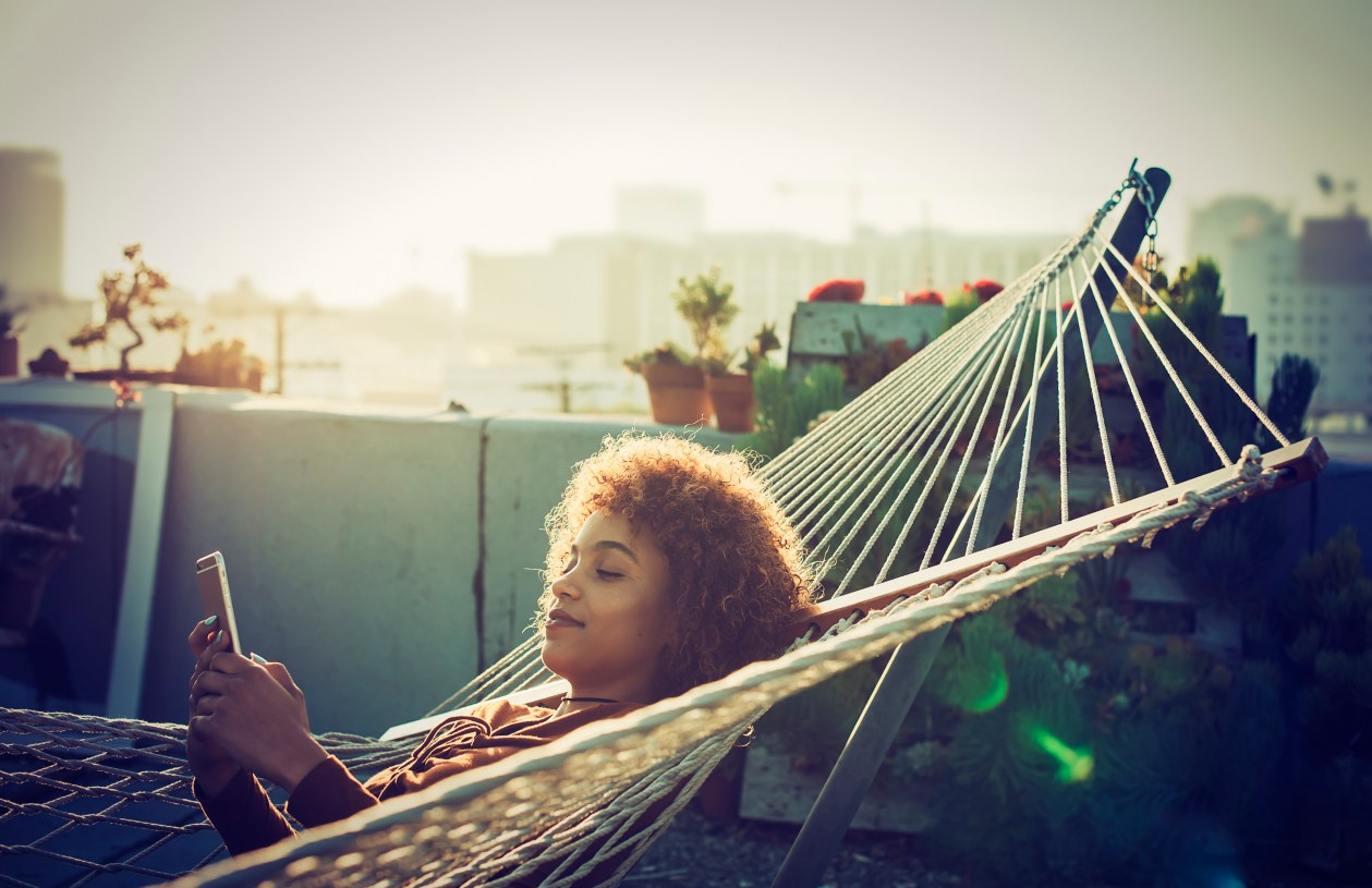 A woman sits outside looking at her phone in a hammock