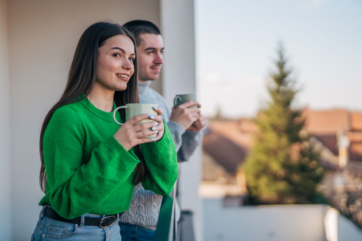 Young woman stands on her apartment balcony with cup of coffee, comparing home loan options for her next residence.