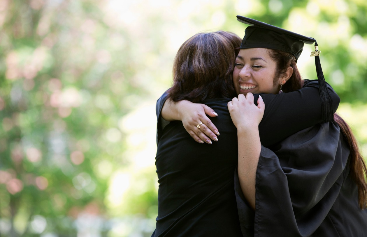 A woman in a graduation outfit hugs her mom