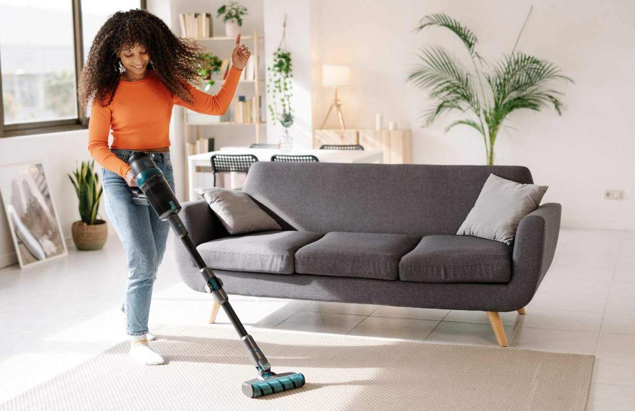 Woman stands in the living room and cleans a carpet on the tiled floor with a vacuum