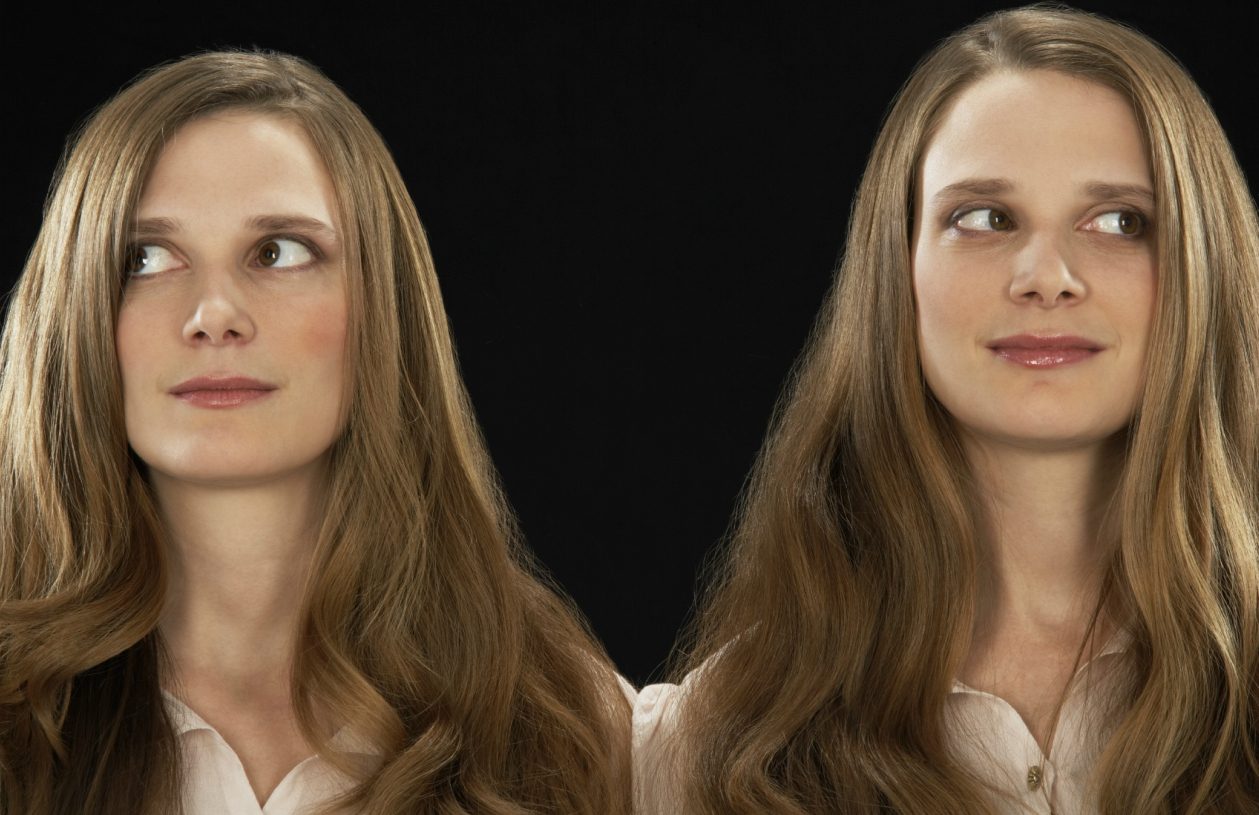 two women with long brown hair who are identical twins look to the side
