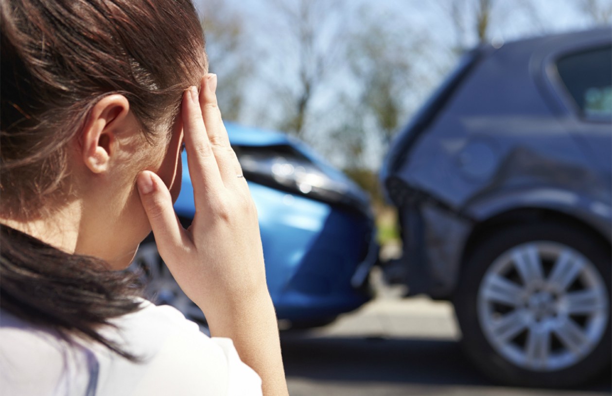 A woman looks at her car that was just in an accident and wonders if she purchased enough additional car insurance
