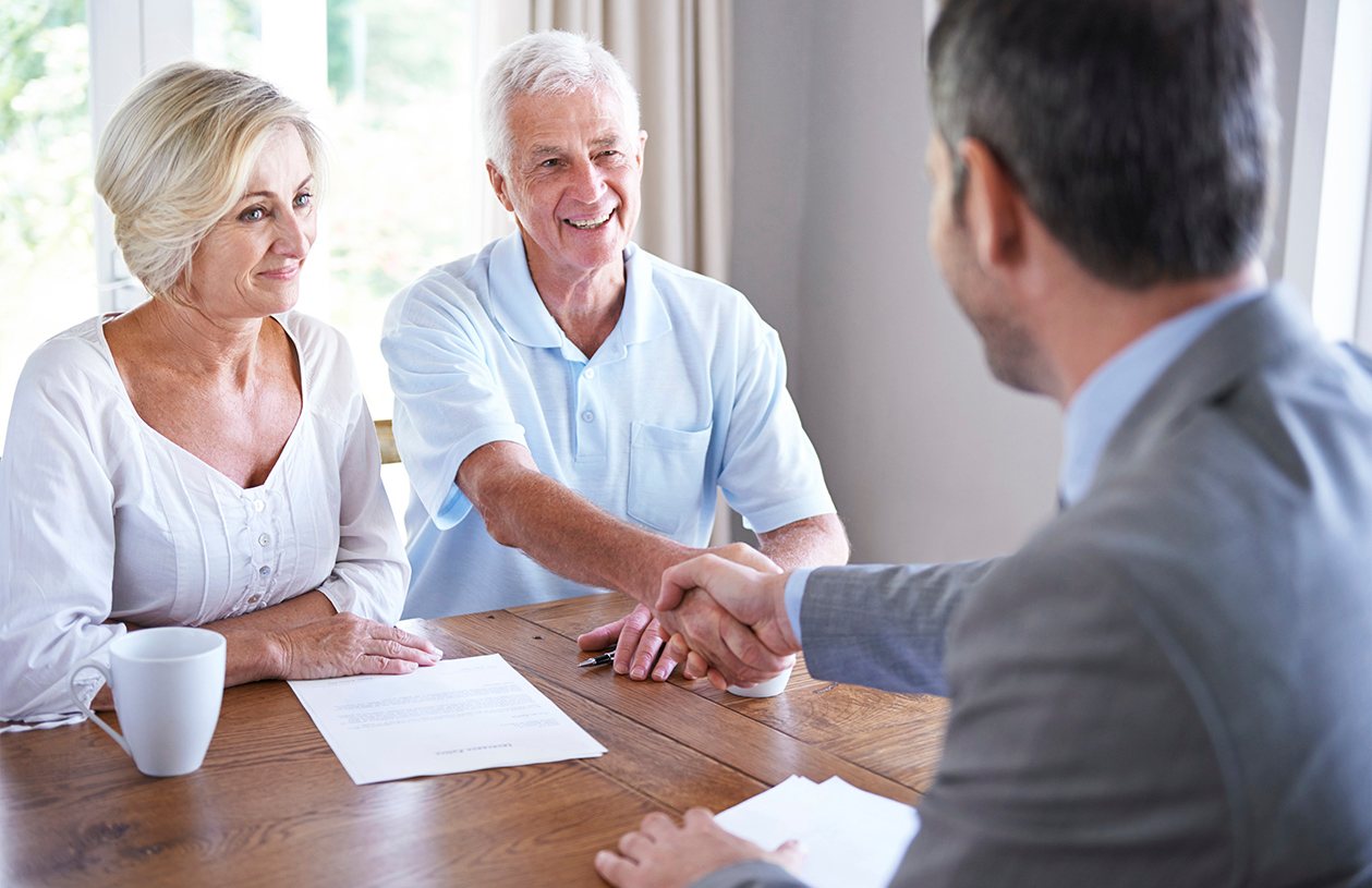 man shaking hands with his financial advisor sitting next to his wife at the dining room table
