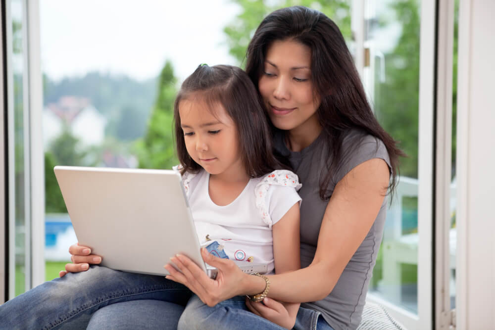 mother showing daughter how to save on laptop computer