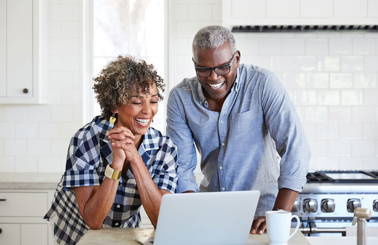 Older couple in their kitchen looking at a laptop planning for early retirement