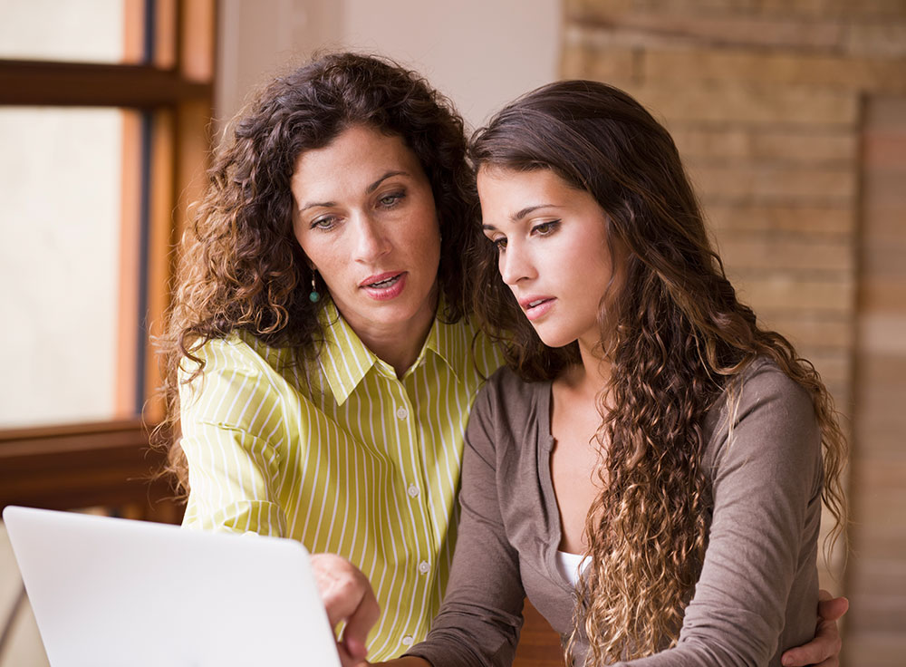 mother showing teen daughter how to save on laptop computer