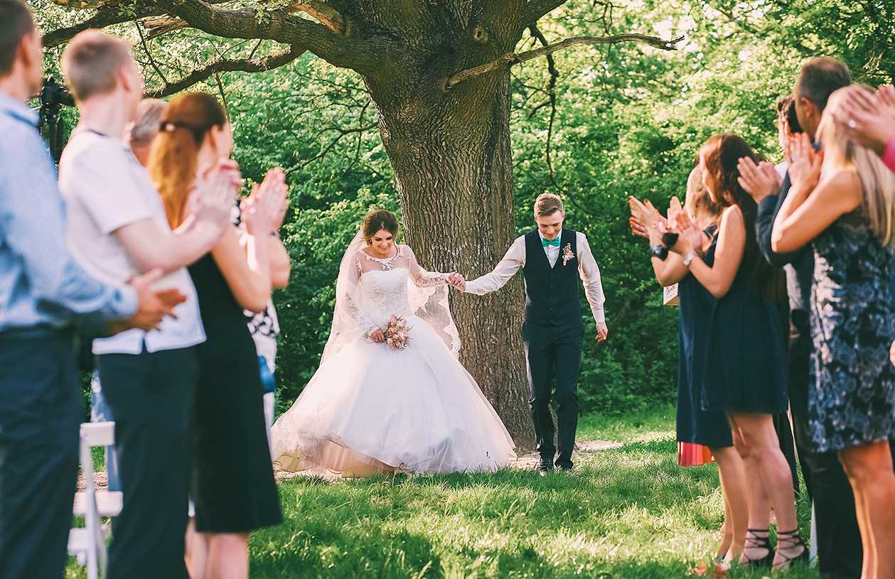 bride and groom holding hands underneath a tree at their outdoor wedding
