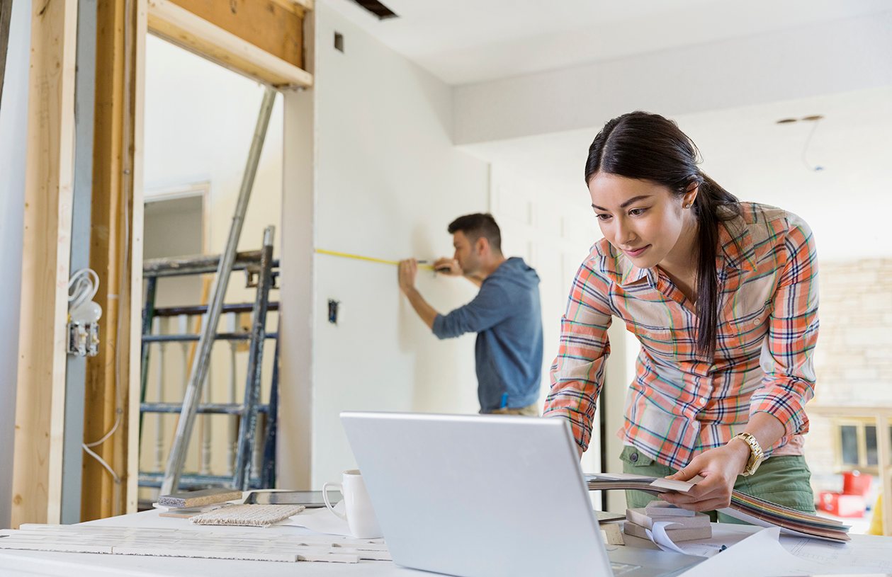 Couple doing some home remodeling while the woman looks at her laptop to help them finance the project